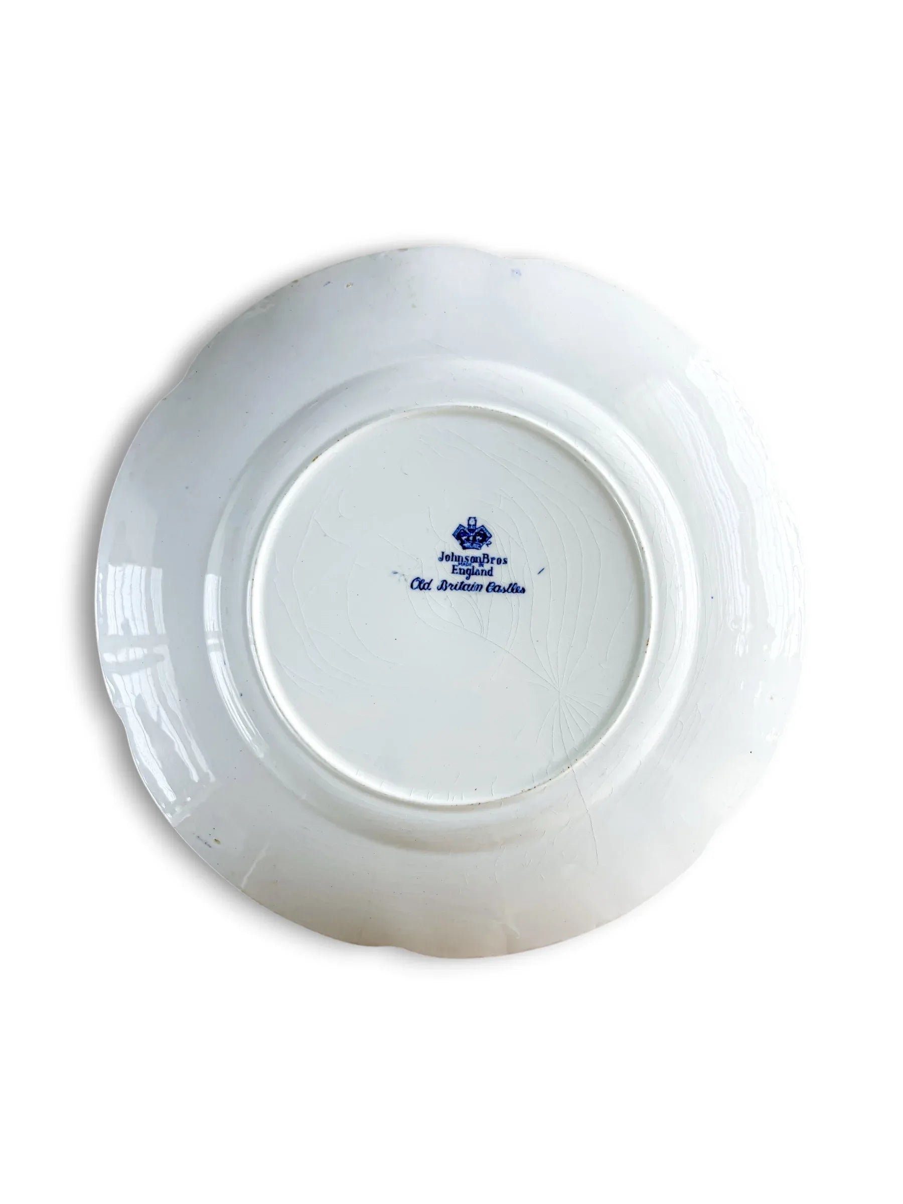 The underside of a Johnson Bros England ironstone plate showing the blue crown backstamp and scalloped rim shape.