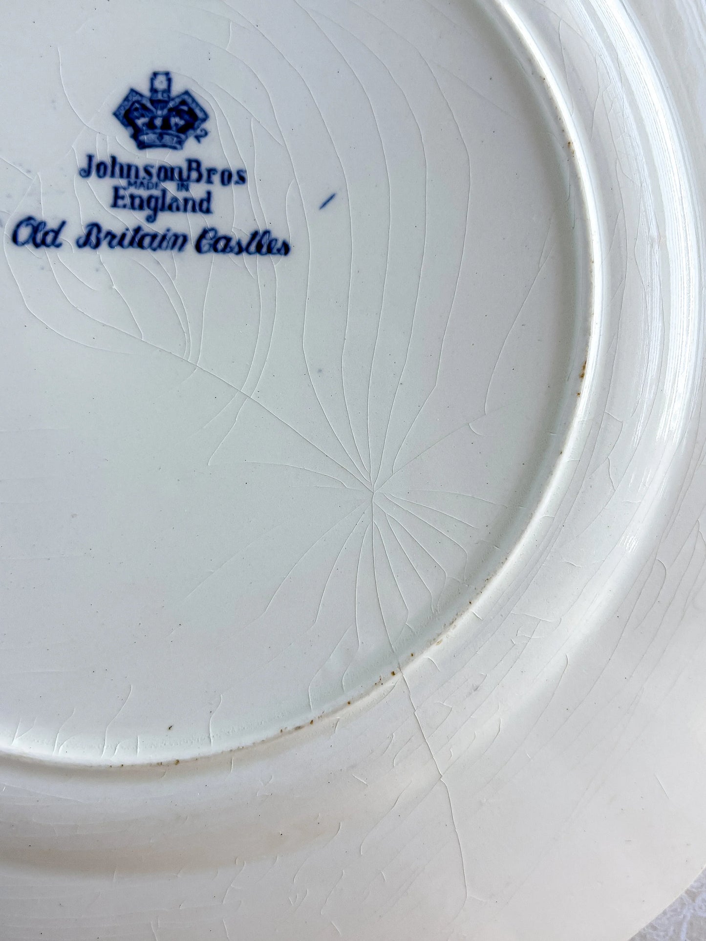 Macro view of authentic glaze crazing and a faint hairline crack on the reverse of a vintage English ironstone plate.
