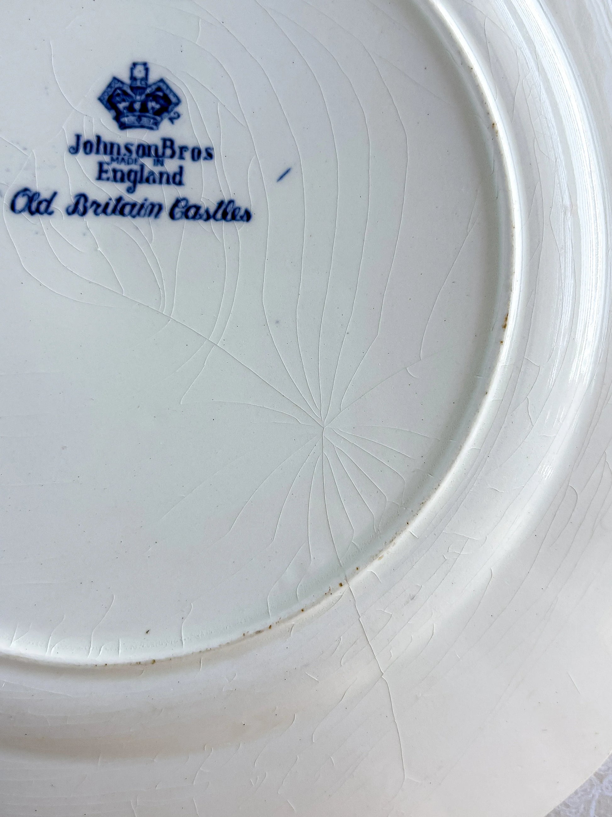 Macro view of authentic glaze crazing and a faint hairline crack on the reverse of a vintage English ironstone plate.