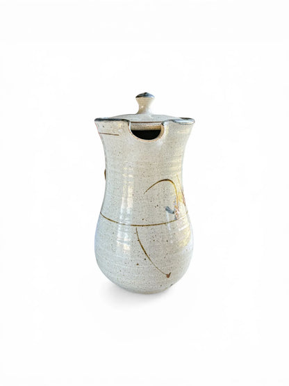 A close-up profile of the Kolonyama server highlighting the pinched, drip-free pouring spout and the fitted lid with a visible steam vent. The high-contrast lighting emphasises the organic, speckled texture of the high-fired stoneware.