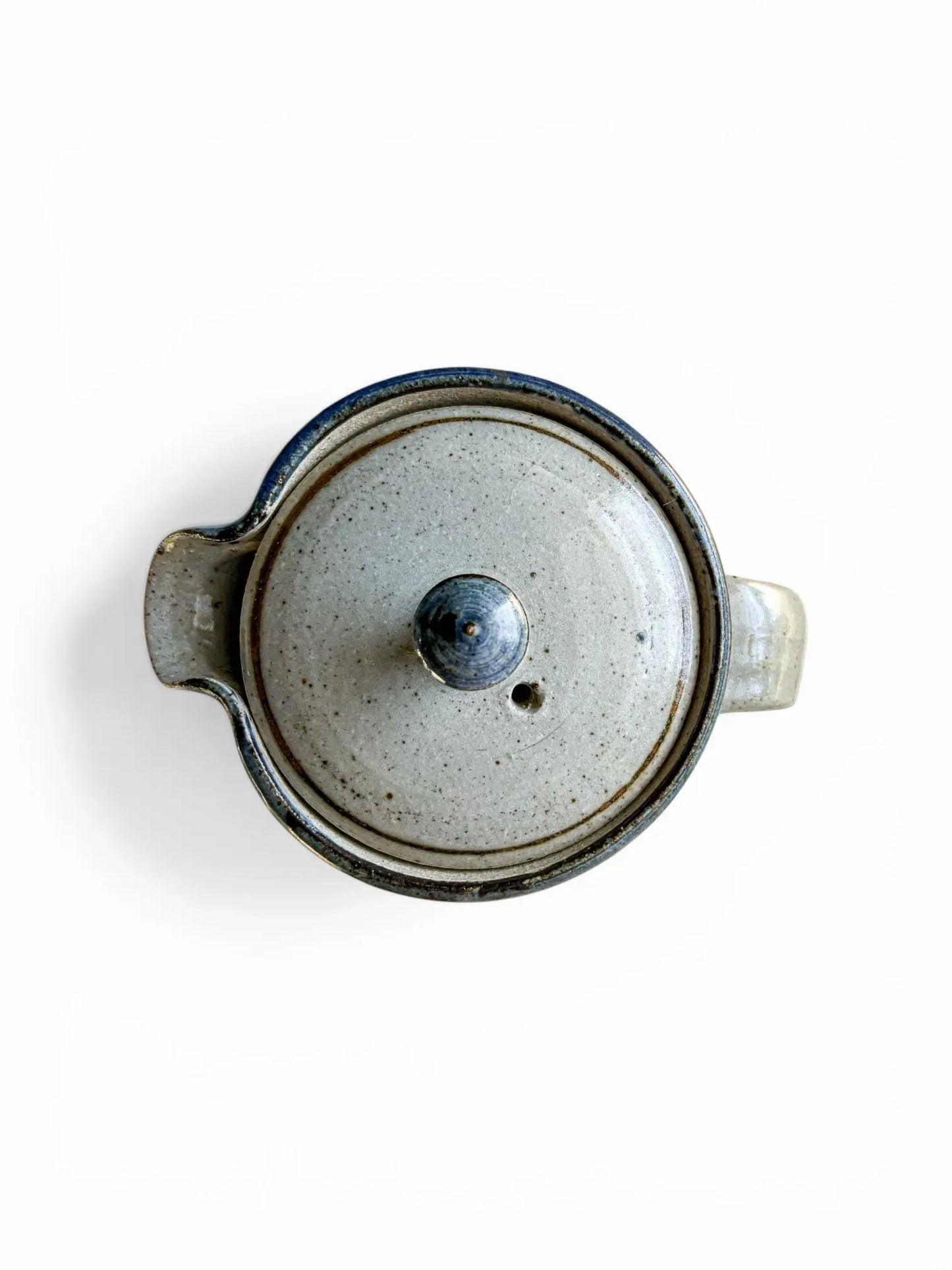 A detailed top-down photograph of the Kolonyama lidded server with the lid removed, revealing the clean, glazed internal cavity of the stoneware. The fitted lid sits beside the rim, showcasing the subtle blue rim detail and the pristine condition of the ceramic joins.