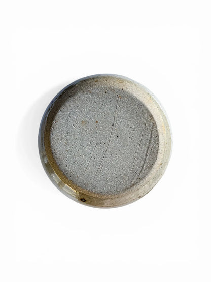 A view of the underside of the vintage lidded server. It displays the raw, unglazed, wire-cut grey stoneware clay base, featuring characteristic firing imperfections and the absence of a maker's mark, confirming its handmade studio pottery origin.