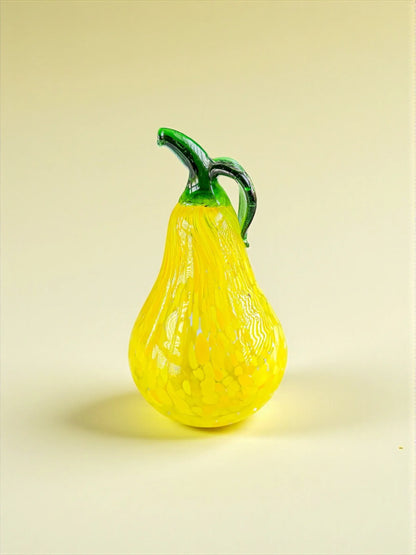 Decorative yellow glass pear with green stem and handle on beige background