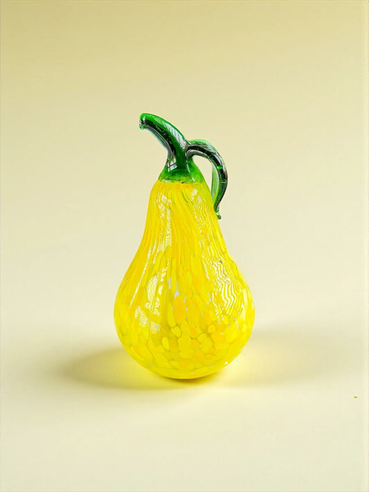 Decorative yellow glass pear with green stem and handle on beige background
