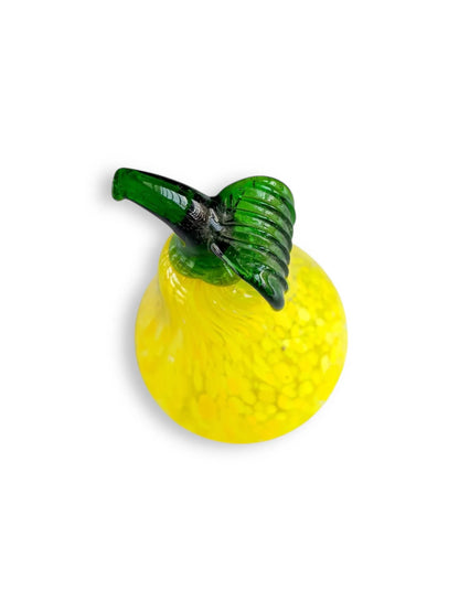 Yellow glass pear ornament with green glass stem and leaf on white background