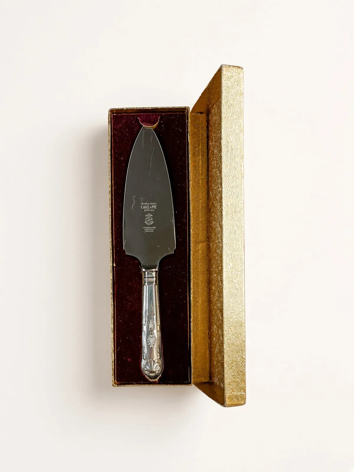 Vintage Lewis Rose Larko stainless steel cake and pie server in its original open gold presentation box with burgundy velvet lining, photographed from above on a cream background.