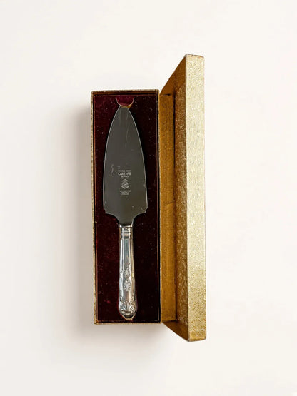Vintage Lewis Rose Larko stainless steel cake and pie server in its original open gold presentation box with burgundy velvet lining, photographed from above on a cream background.