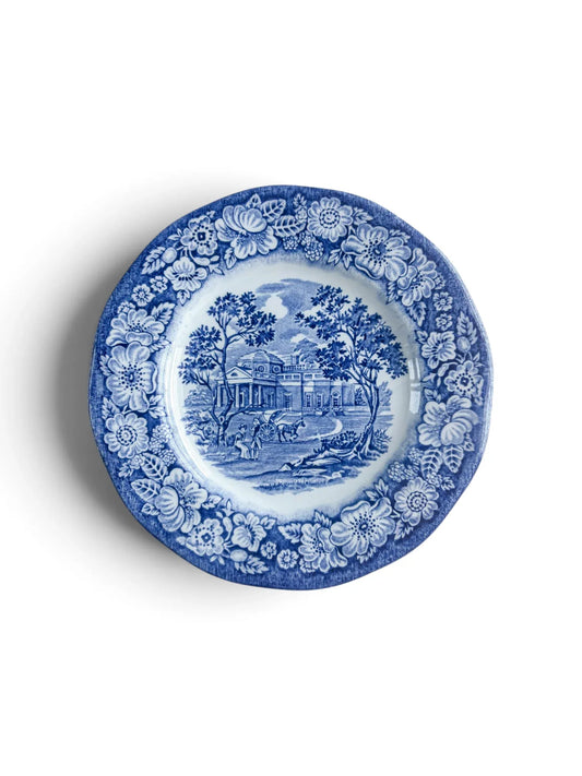 Liberty Blue Staffordshire ironstone bread and butter plate, 15.1 cm, showing the Monticello scene in cobalt transferware with a floral rose border, photographed from above on a white background.
