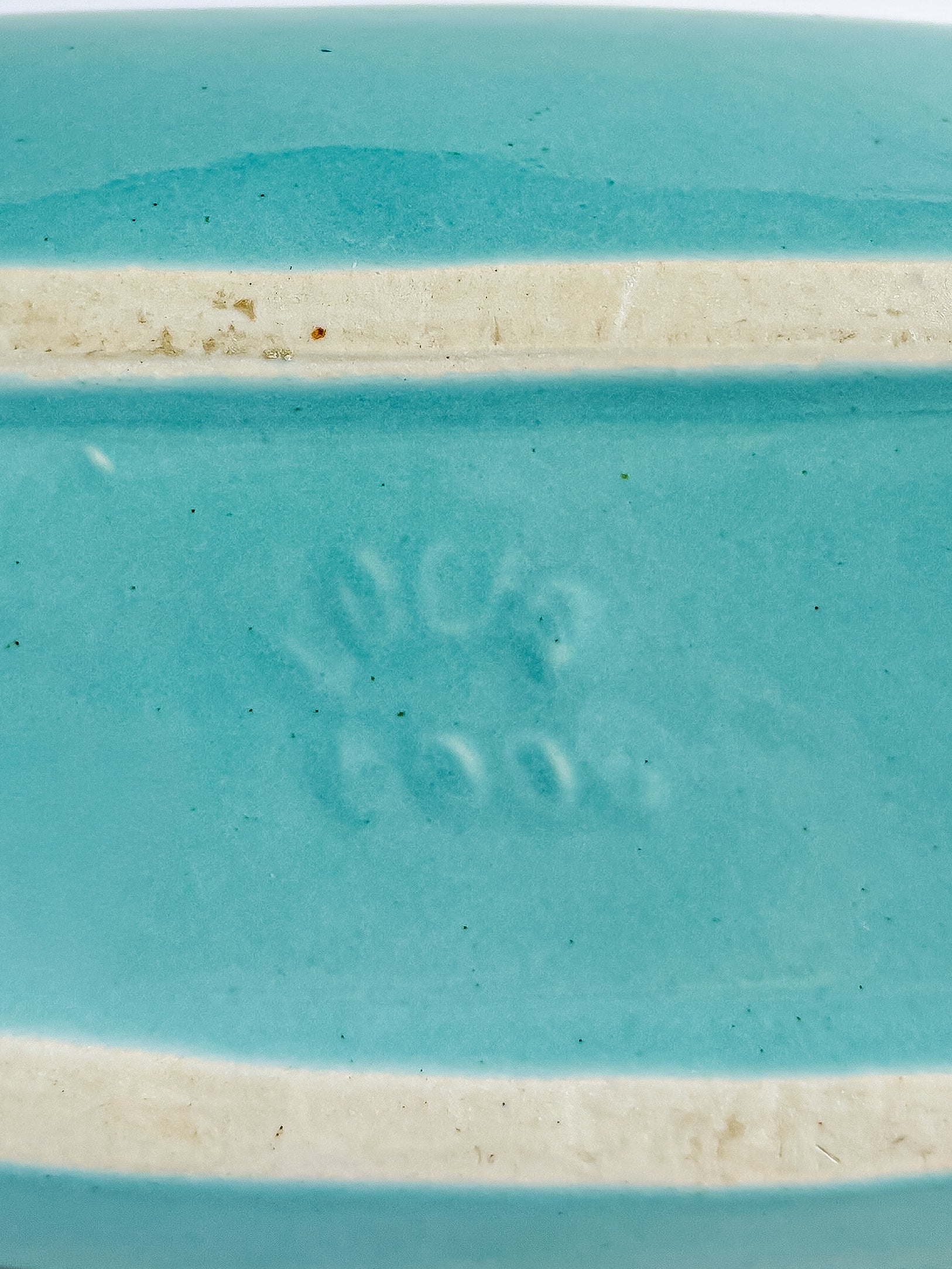 Close-up of turquoise ceramic piece with embossed maker's mark and unglazed foot ridge