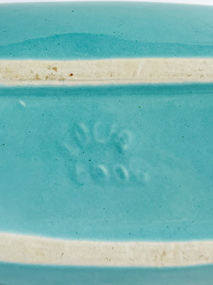 Close-up of turquoise ceramic piece with embossed maker's mark and unglazed foot ridge