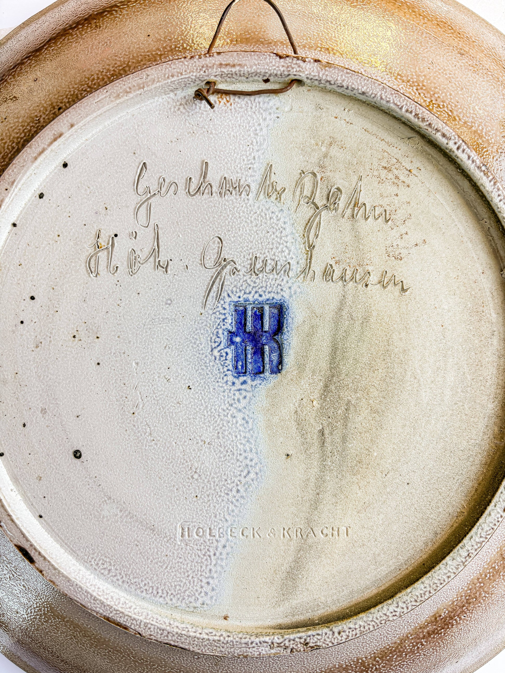 Handwritten cursive Geschwister Bahn Höhr-Grenzhausen signature on reverse of ceramic charger along with the Embossed HK workshop mark and Holbeck and Kracht gallery stamp on vintage pottery base.
