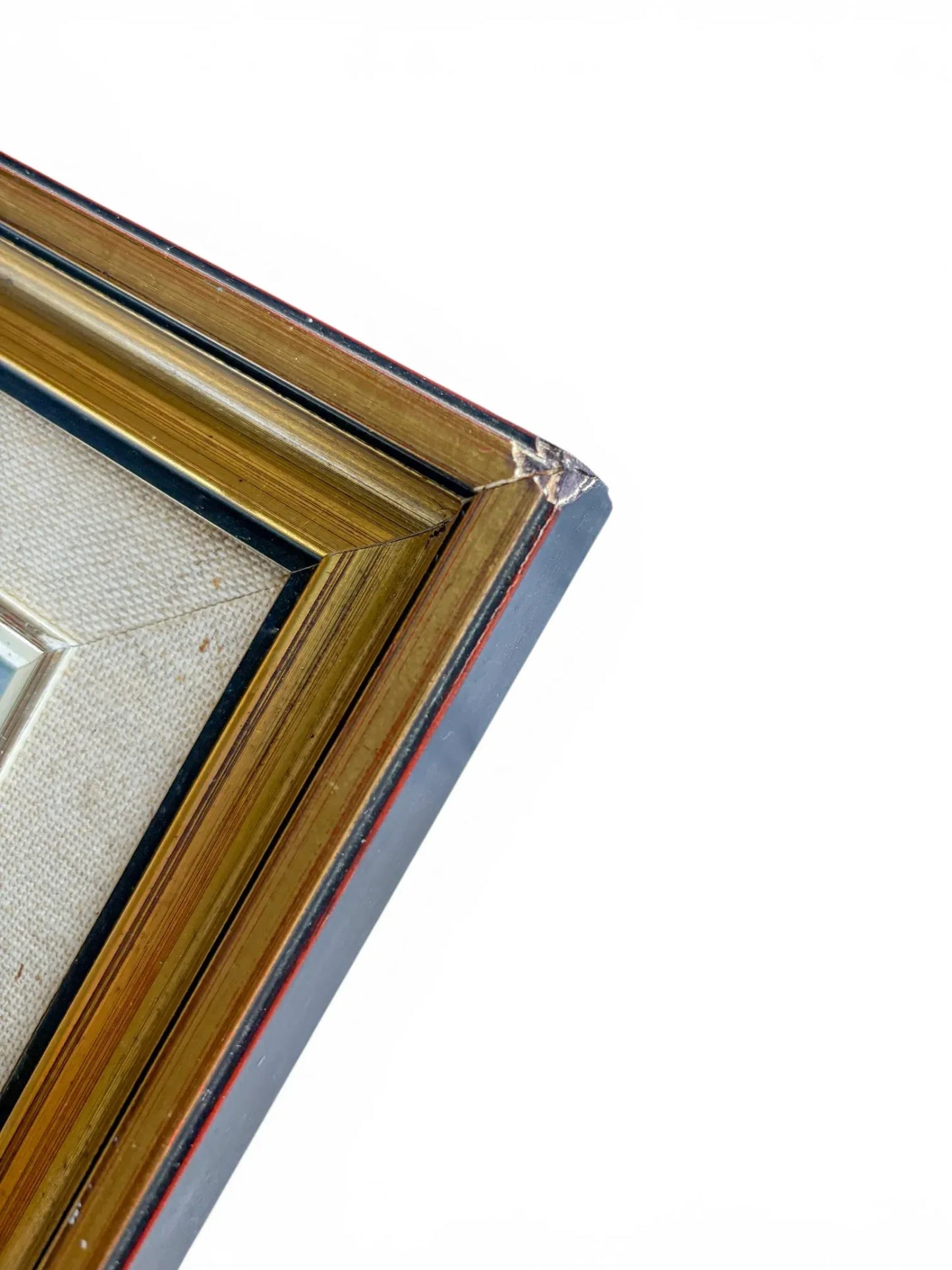 A detailed top-down view focused on the corner mitre joint of a vintage gold picture frame against a plain white backdrop. The macro shot highlights minor cracking, chipping, and natural rubbing to the aged gilt finish at the frame's edge.