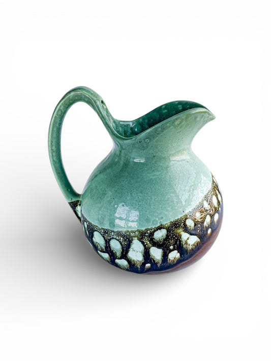 Handcrafted ceramic pitcher with green glaze and textured dark blue and white pattern