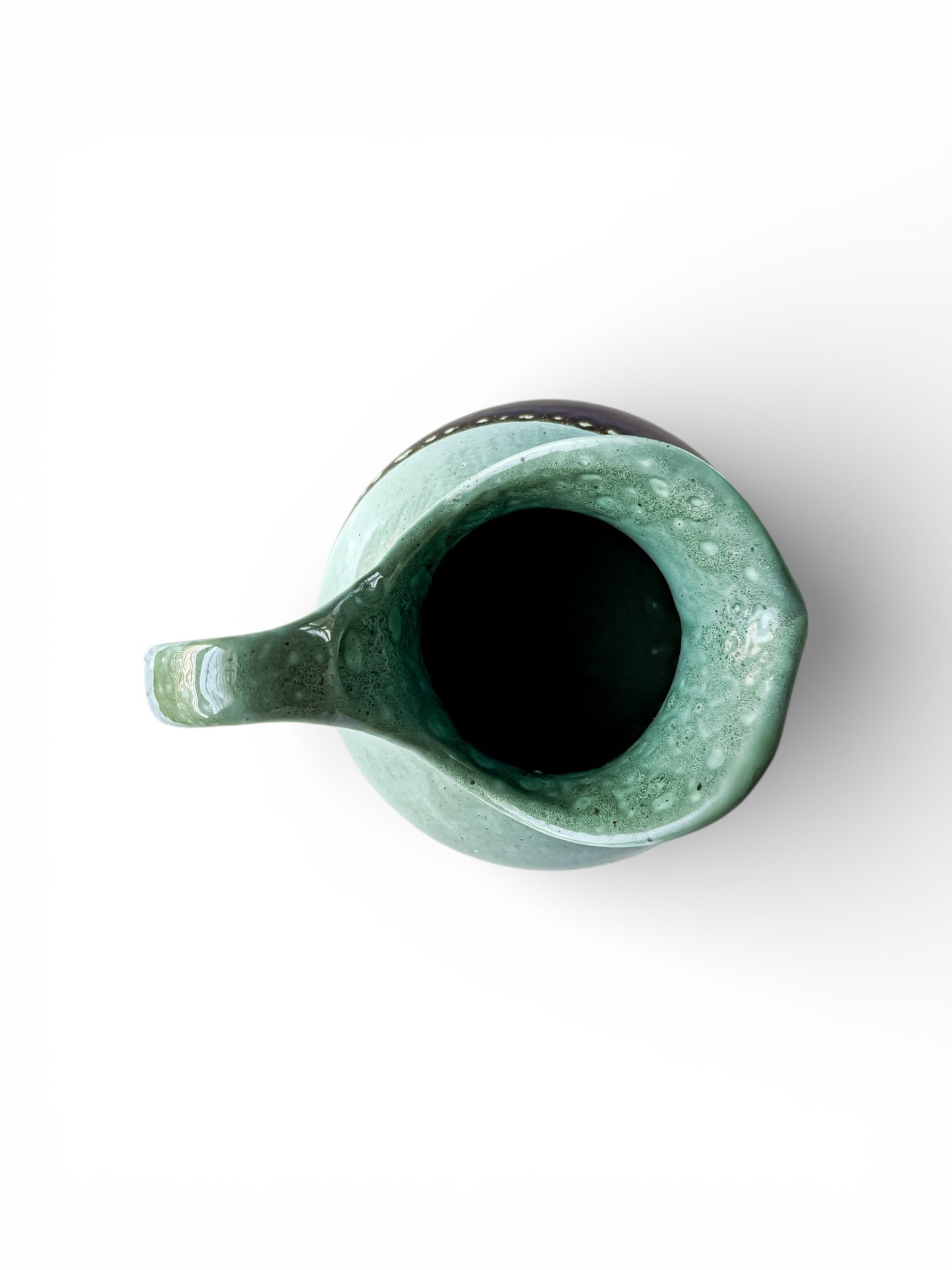 Top view of a green glazed ceramic pitcher with a spout and handle on white background