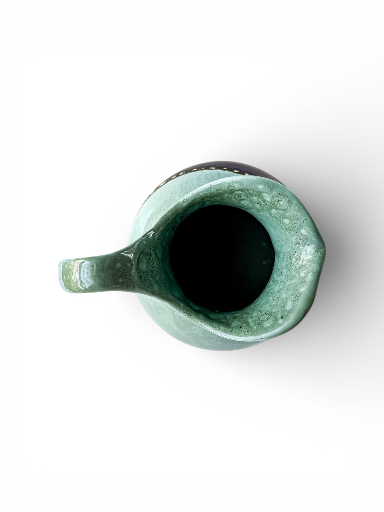 Top view of a green glazed ceramic pitcher with a spout and handle on white background