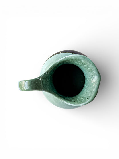 Top view of a green glazed ceramic pitcher with a spout and handle on white background