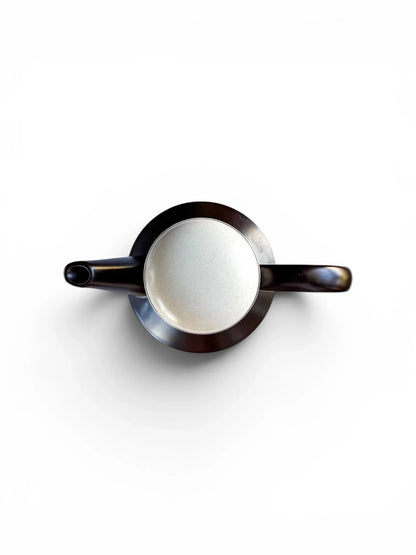 Top-down view of a Midwinter Stonehenge coffee pot. The symmetrical composition shows the dark brown spout and handle extending from the cylindrical body, with the speckled light-coloured lid centred at the top.