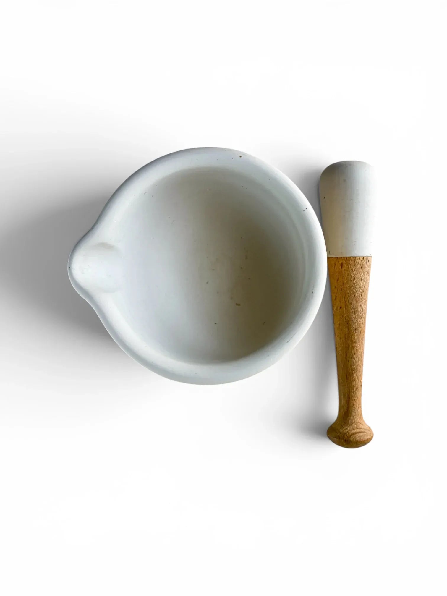 Overhead flat-lay view of a white ceramic Milton Brook mortar bowl with a pouring spout alongside its porcelain-headed wooden pestle on a solid white background.
