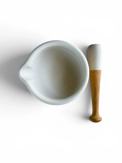 Overhead flat-lay view of a white ceramic Milton Brook mortar bowl with a pouring spout alongside its porcelain-headed wooden pestle on a solid white background.