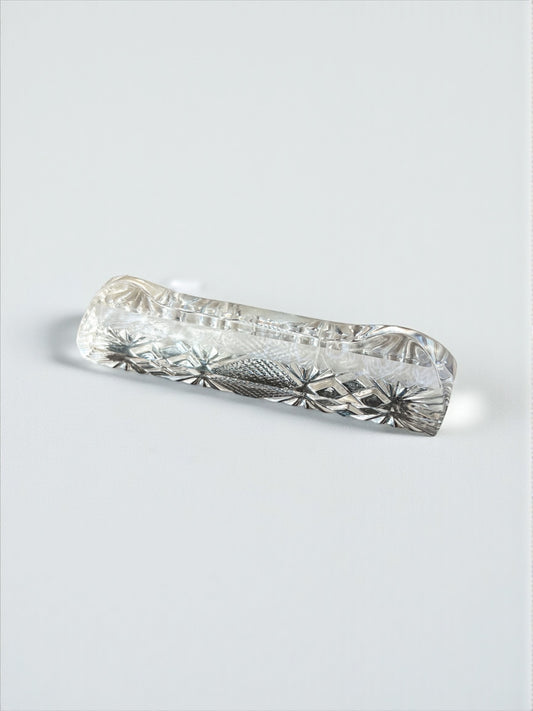 Clear crystal chopstick rest with intricate starburst engravings on white background