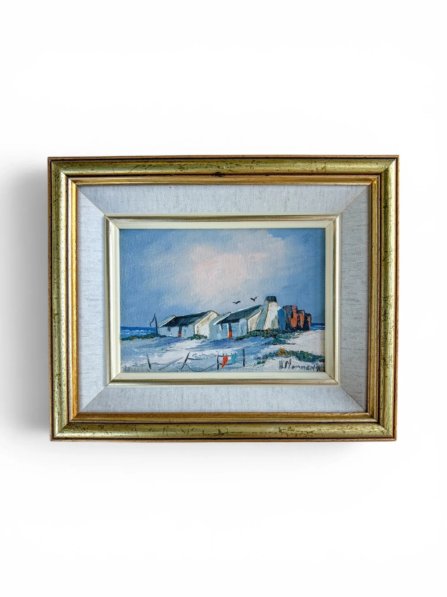 Front studio shot of a 1996 original coastal landscape oil painting by H. Mommen against a clean white background. The textured impasto artwork portrays South African West Coast cottages nestled in sand dunes by the sea, complete with its vintage gold frame and off-white linen inner border.