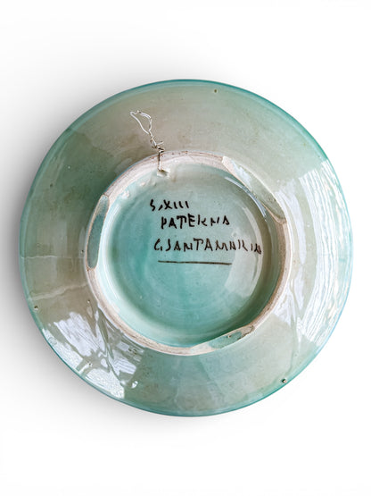Bottom view of vintage turquoise glazed ceramic plate with handwritten markings and wire hanger