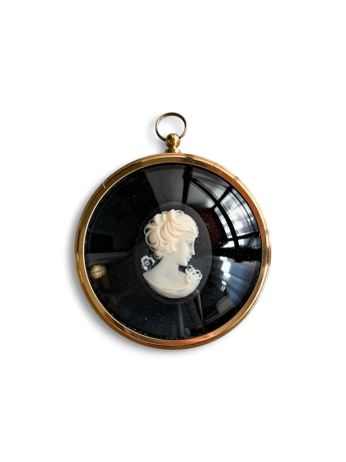 A round gilt-framed Peter Bates cameo of a lady in profile, hair dressed high and flowers at the shoulder, in white relief on a black ground, with a hanging ring.