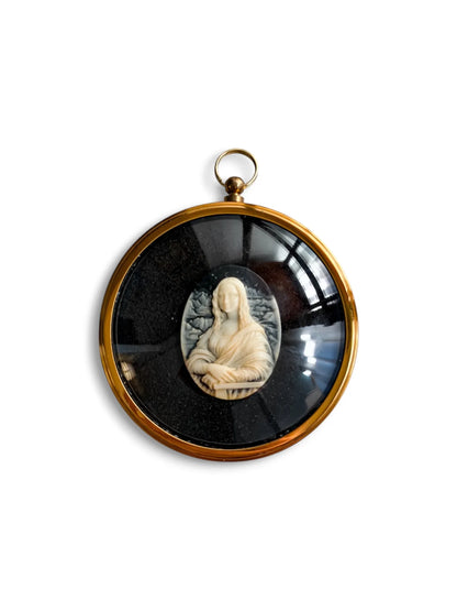 A round gilt-framed Peter Bates cameo of the Mona Lisa, hands folded on the chair rail, in white relief on a black ground, with a hanging ring.