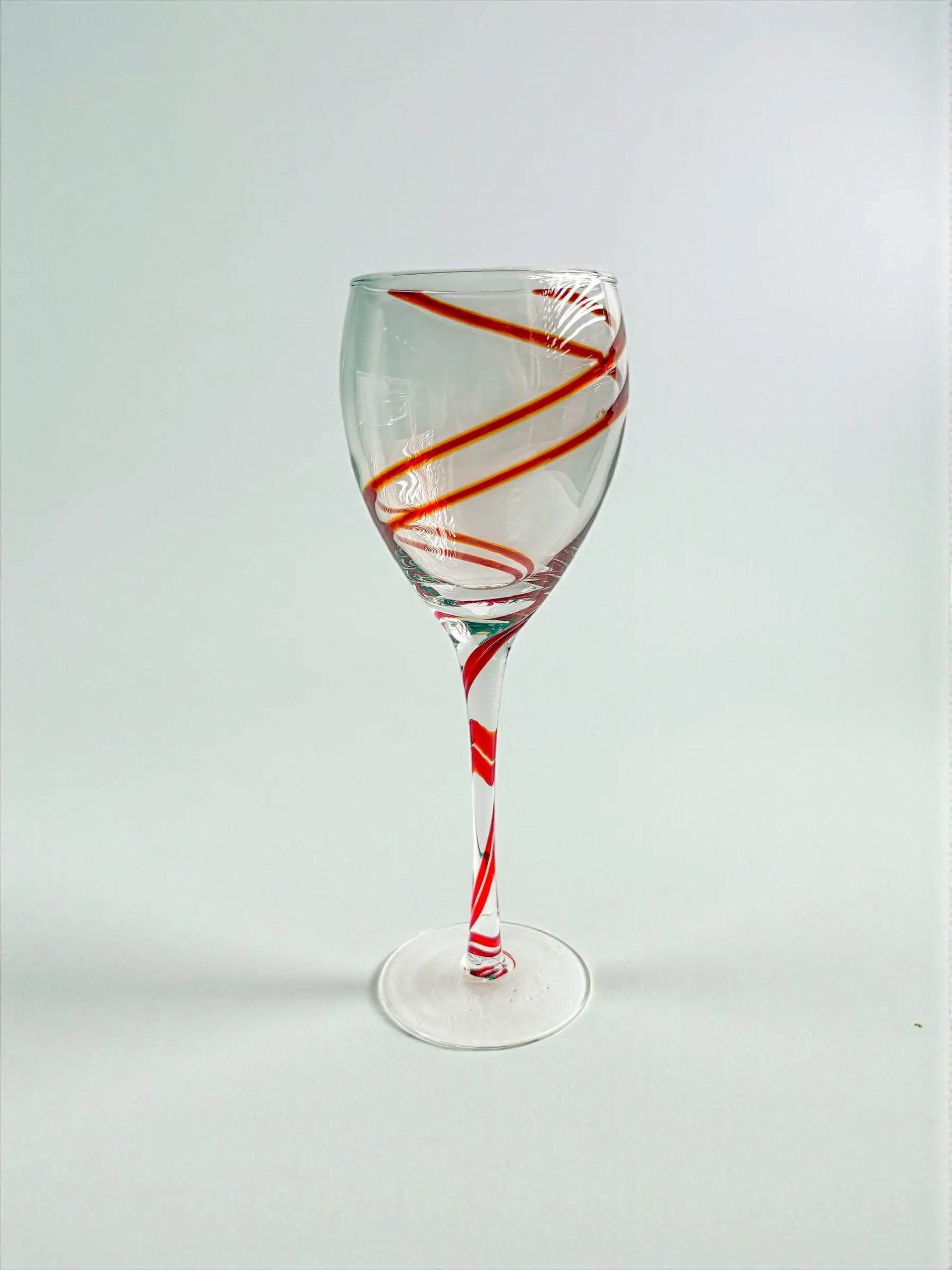Clear wine glass with red orange spiral stripe design on bowl and stem against white background