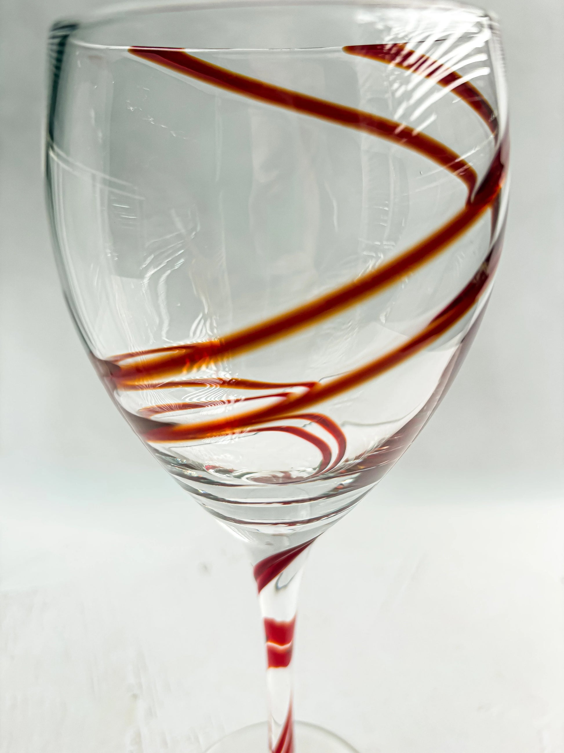 Close-up of a clear wine glass with red spiral swirl decoration on the bowl and stem