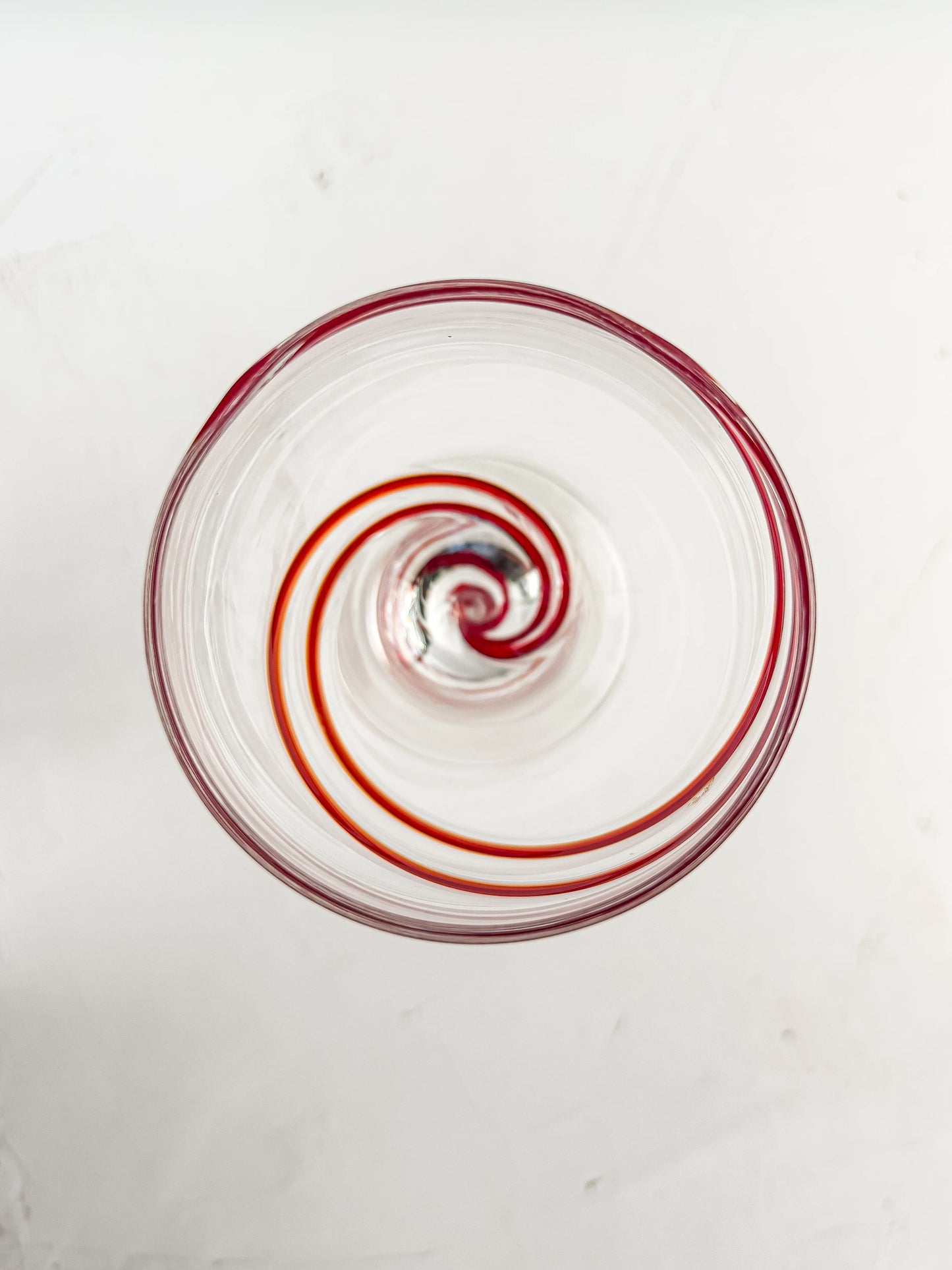 Top view of a clear glass with a red spiral design inside on a white surface