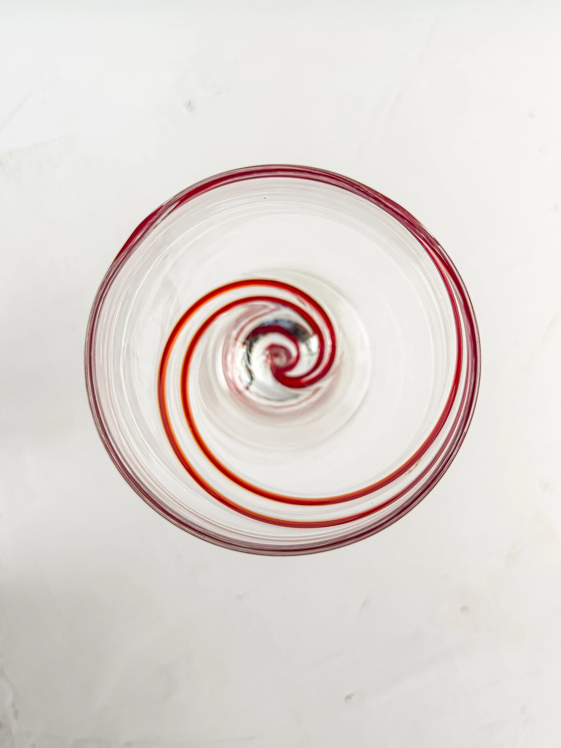 Top view of a clear glass with a red spiral design inside on a white surface
