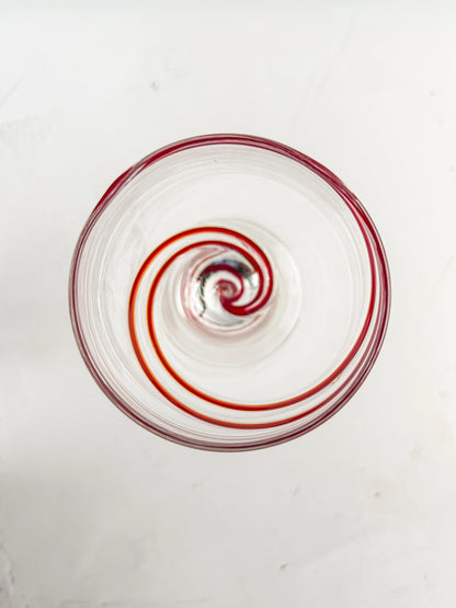 Top view of a clear glass with a red spiral design inside on a white surface