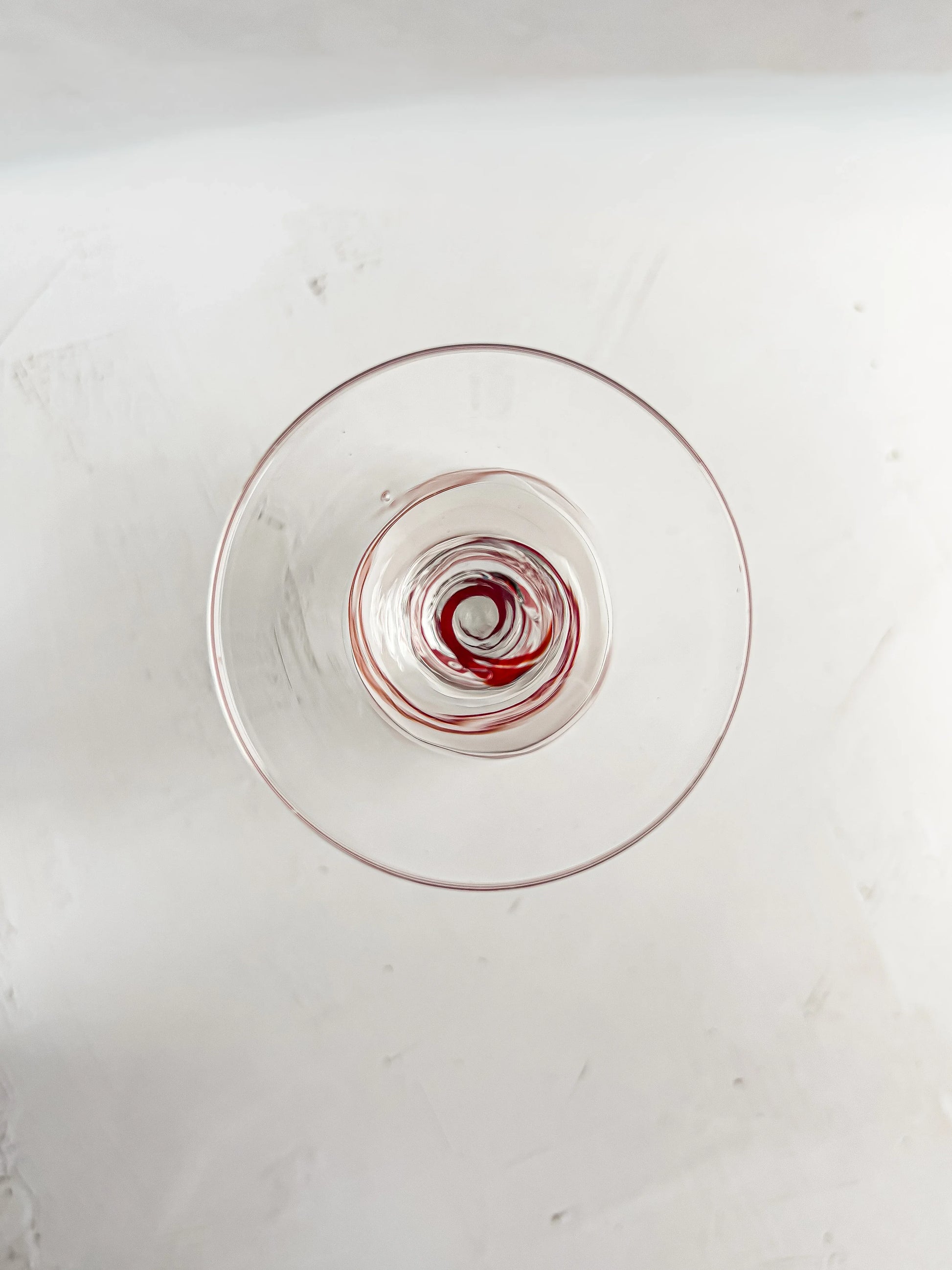 Top view of a clear glass with red wine residue swirled at the bottom on a white surface