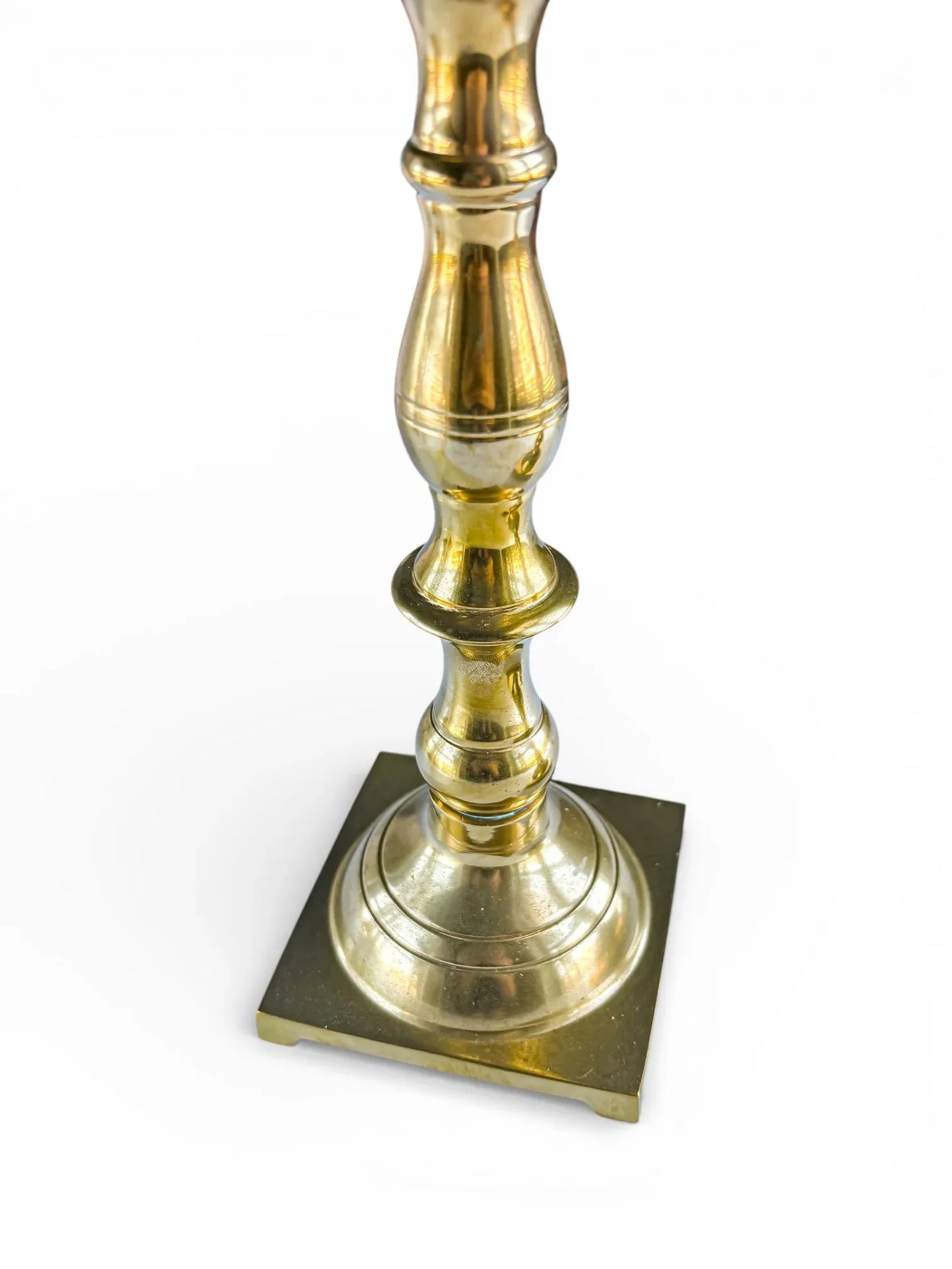 Polished vintage brass candlestick with ornate stem and square base on white background