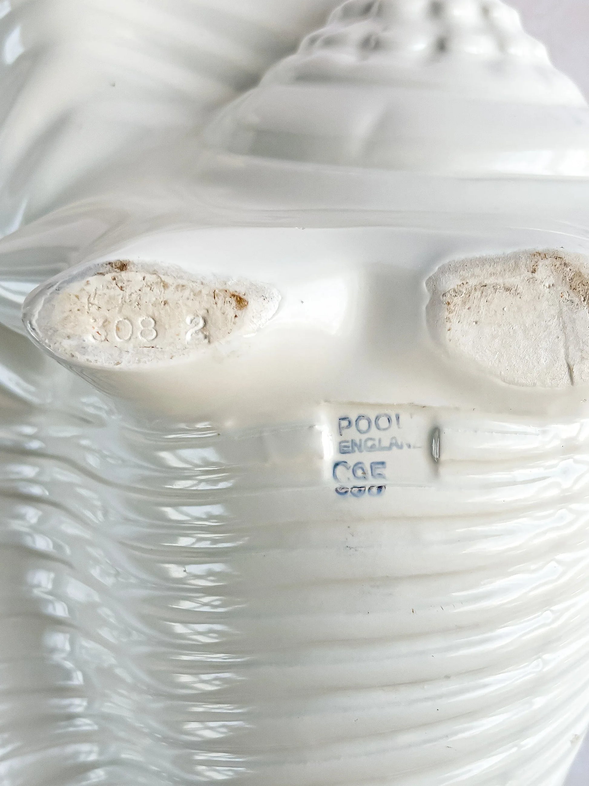 Close-up of white porcelain shell figurine base marked with 'Poole England' and model numbers