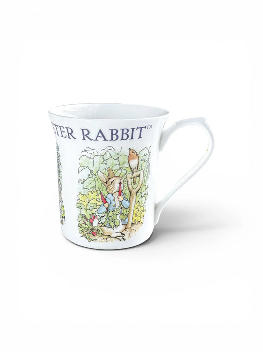 Beatrix Potter Peter Rabbit centenary mug featuring Peter in Mr. McGregor’s garden with a robin on a spade.