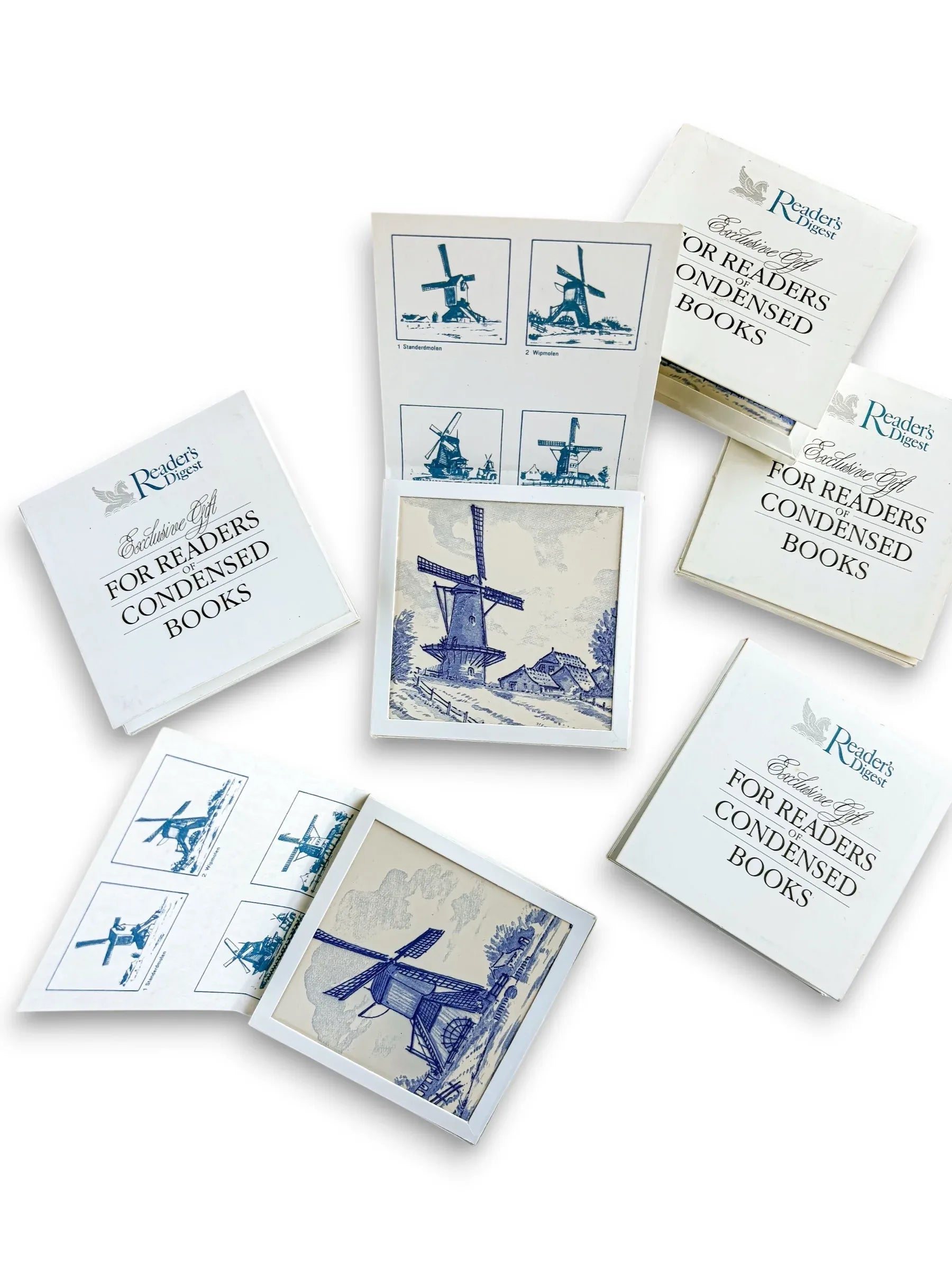 A curated collection of six vintage Regina Delft Blue windmill tiles with original Reader’s Digest Condensed Books presentation sleeves and informational inserts on a clean white background.