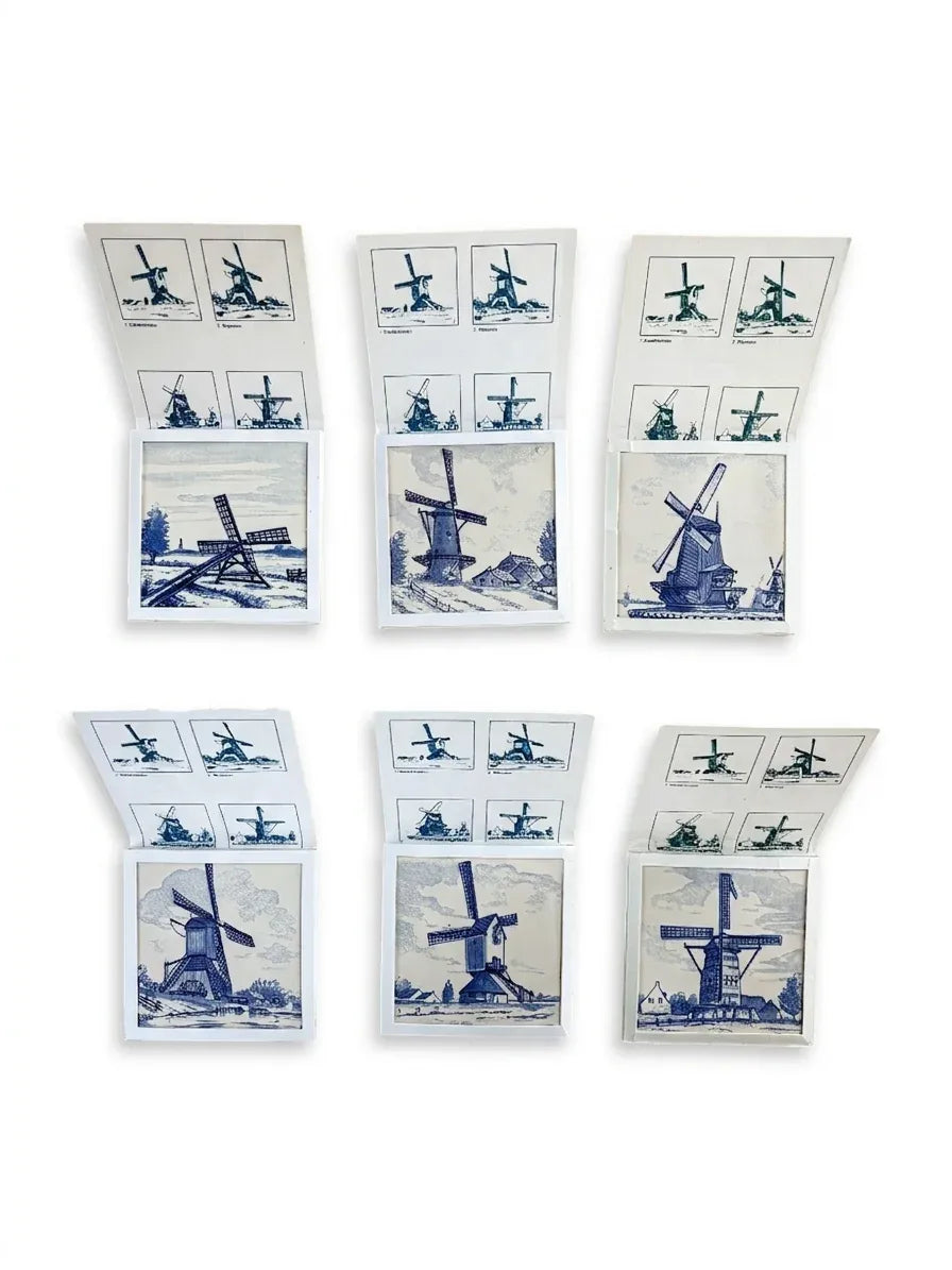 A complete set of six Regina Delft ceramic tiles, each featuring a different traditional Dutch windmill illustration, displayed inside their original white cardboard collector sleeves.