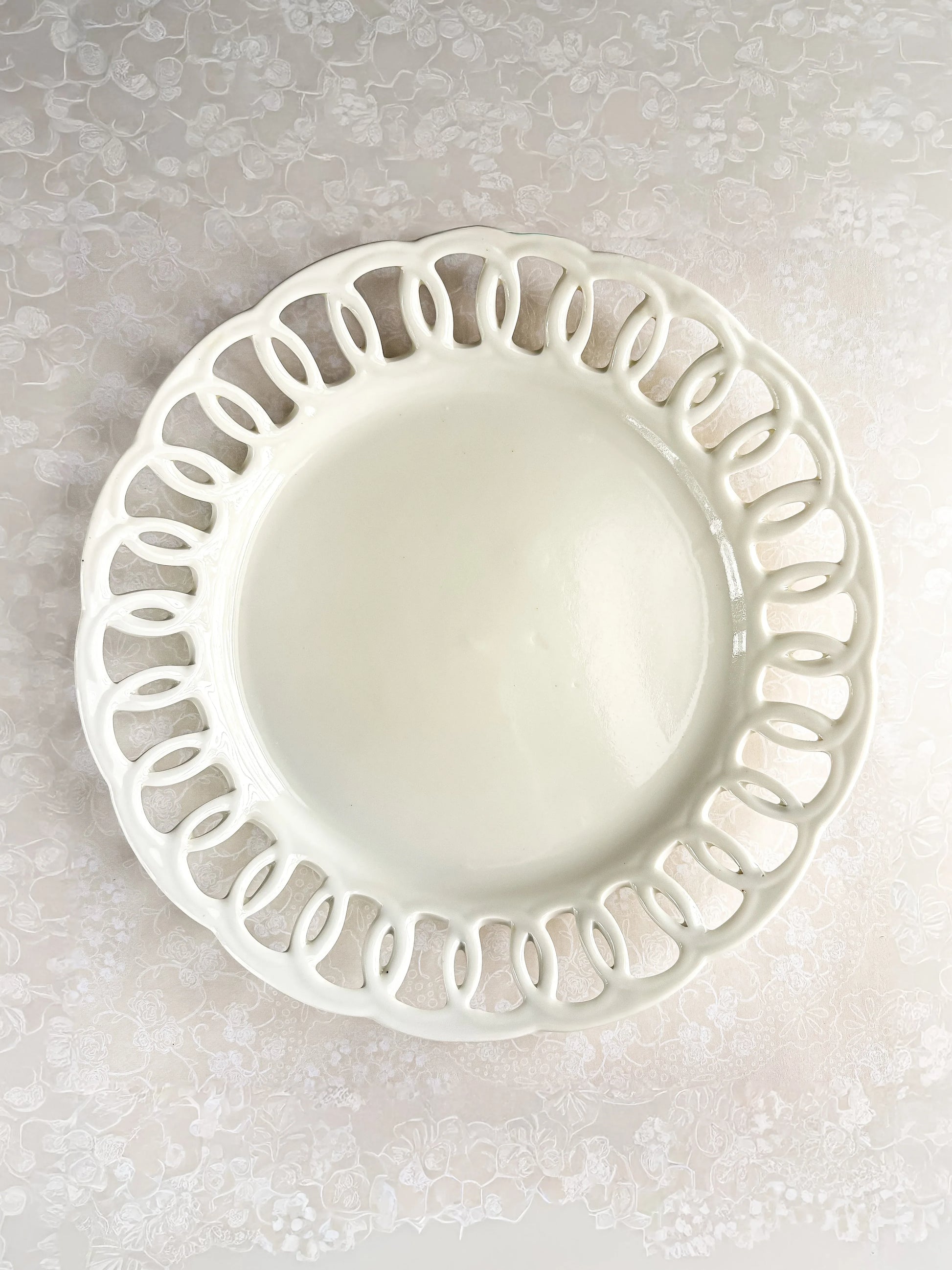 White ceramic plate with decorative cutout rim on floral lace tablecloth