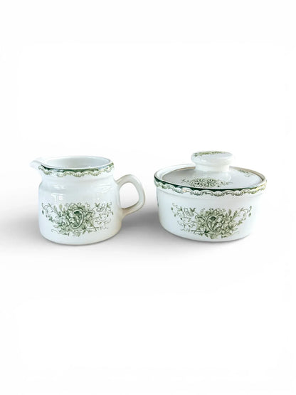 Profile shot of the Rörstrand Grön Anna creamer and lidded sugar bowl set with forest green floral patterns on white flintware.
