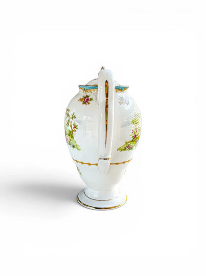 Rear profile view focusing on the elegant, white bone china S-scroll handle. The image shows the bright gold trim tracing the outer curves, the moulded thumb rest, and the floral sprays decorating the shoulder of the pot.