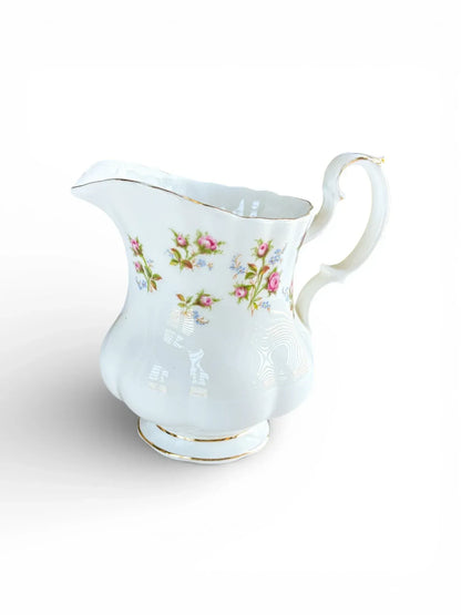 Profile view of a Royal Albert Winsome bone china creamer on the Montrose shape featuring pink rose sprays and a scrolled handle.