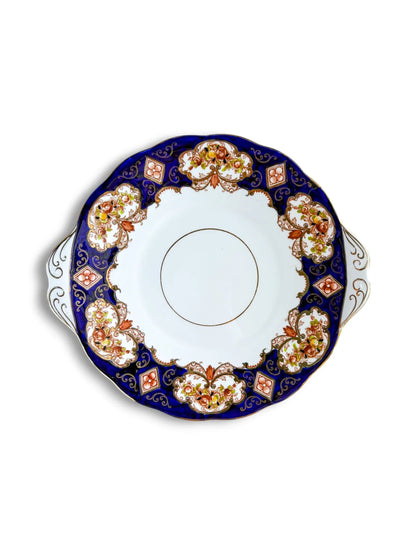 Top-down view of a vintage Royal Albert Heirloom handled cake plate on a clean white background. The design features a deep cobalt blue border with Imari-style burnt orange floral panels and intricate gold filigree.