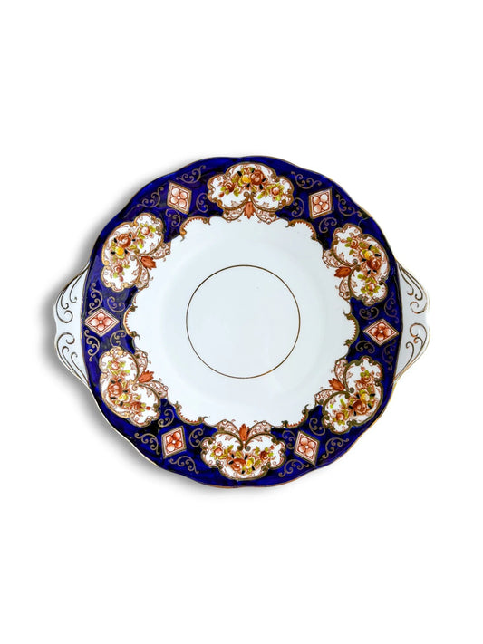 Top-down view of a vintage Royal Albert Heirloom handled cake plate on a clean white background. The design features a deep cobalt blue border with Imari-style burnt orange floral panels and intricate gold filigree.
