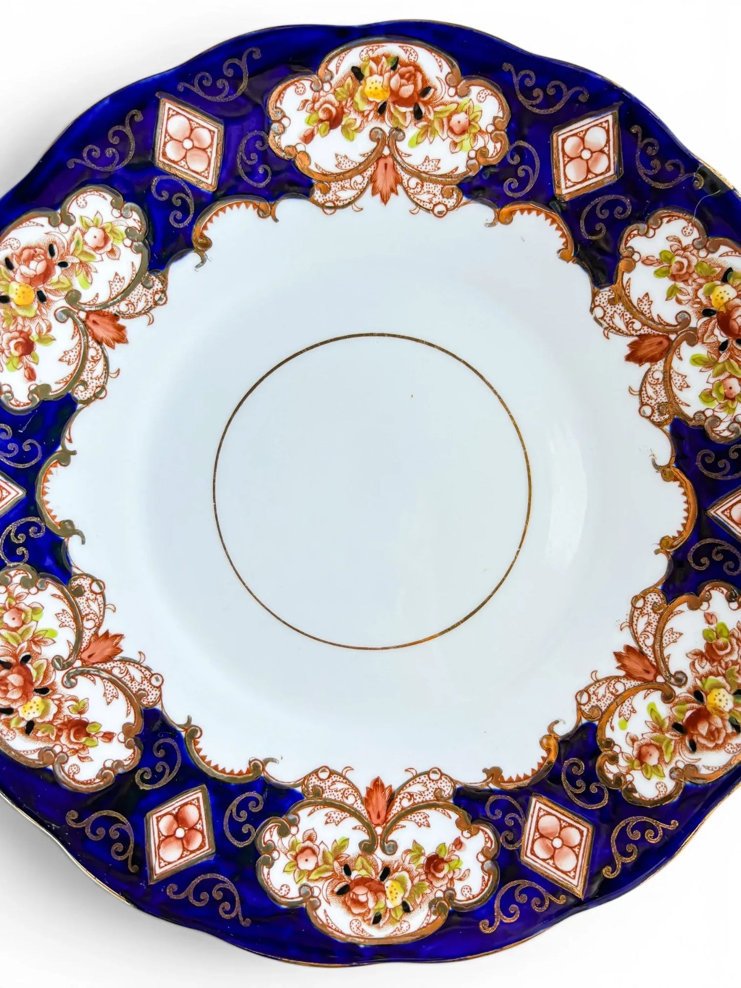 A detailed close-up of the Royal Albert Heirloom pattern, showcasing the vibrant rust-coloured flowers, gold scrollwork, and the rich cobalt blue glaze against the crisp white bone china centre.