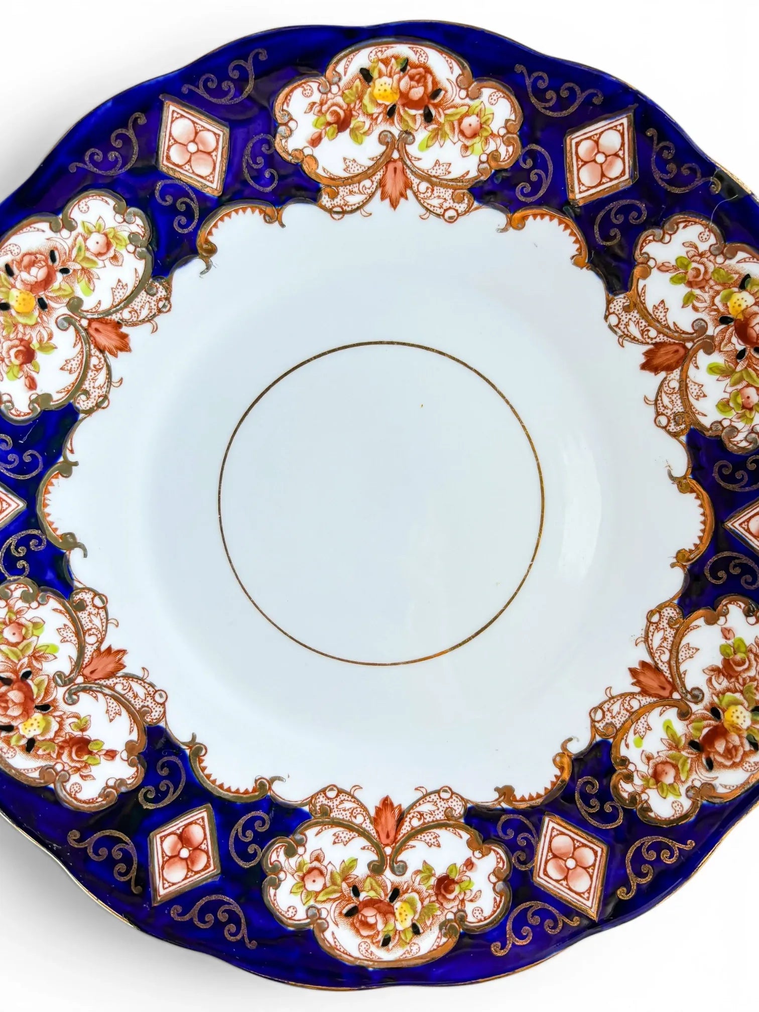 A detailed close-up of the Royal Albert Heirloom pattern, showcasing the vibrant rust-coloured flowers, gold scrollwork, and the rich cobalt blue glaze against the crisp white bone china centre.