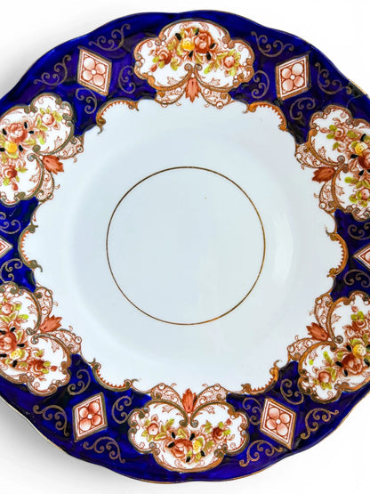 A detailed close-up of the Royal Albert Heirloom pattern, showcasing the vibrant rust-coloured flowers, gold scrollwork, and the rich cobalt blue glaze against the crisp white bone china centre.