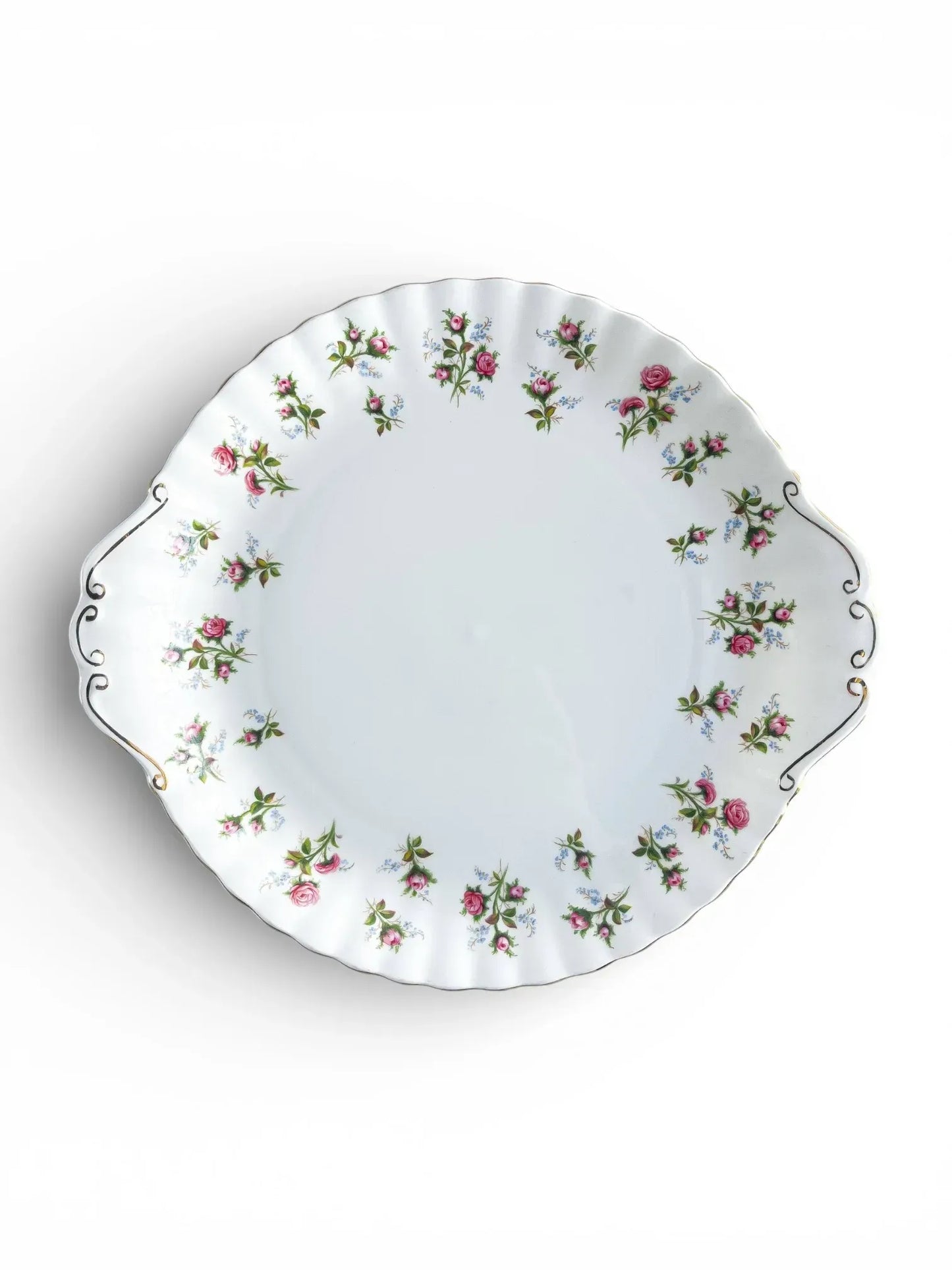 A top-down view of a vintage Royal Albert Winsome round cake plate featuring integrated tab handles and a scalloped edge decorated with pink rose sprays and blue forget-me-nots.