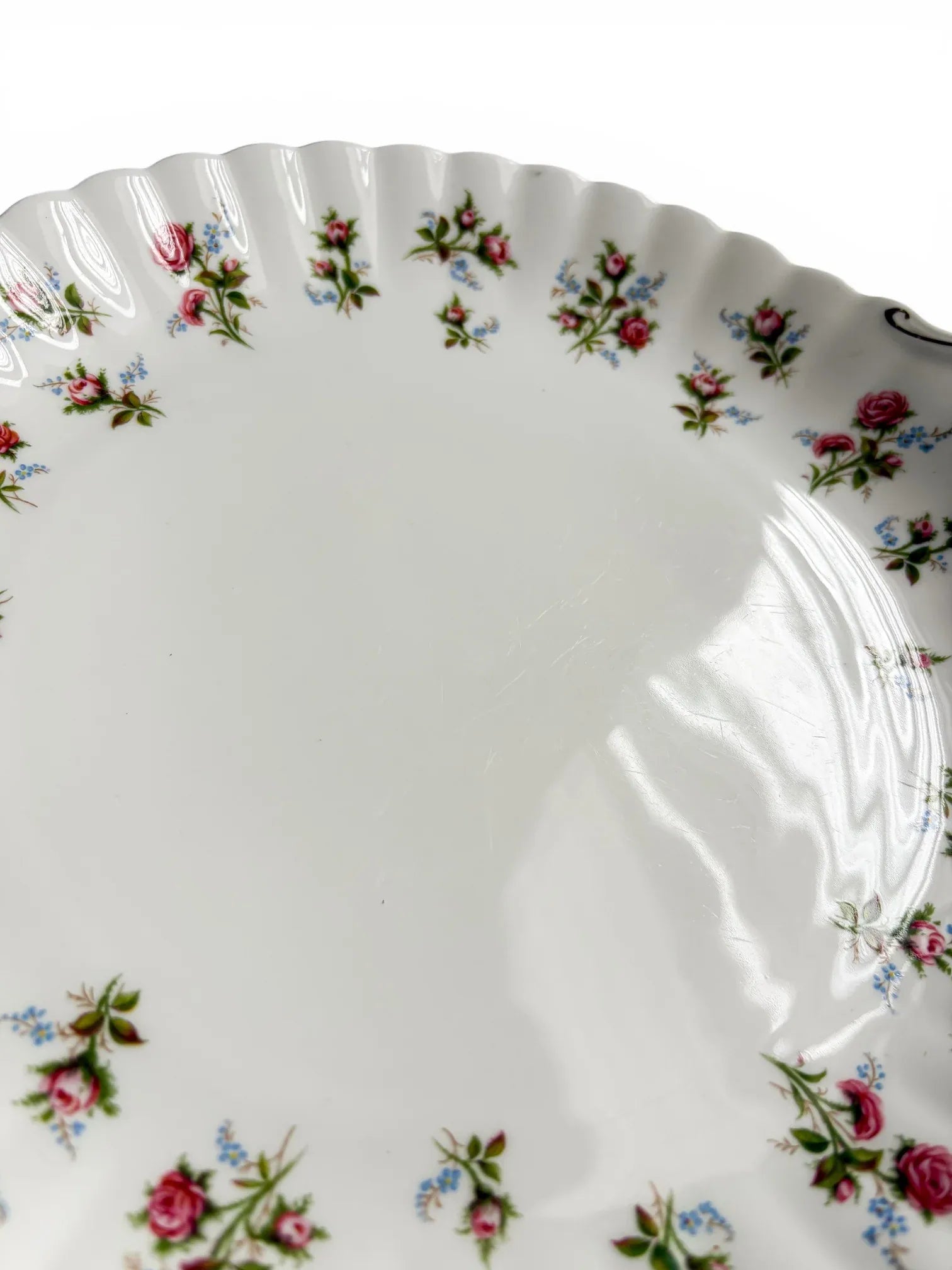 A close-up of the cake plate surface highlighting the light utensil marks and minor gold rubbing on the scalloped rim.